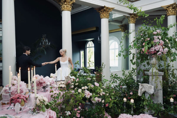 Couple surrounded by pink and white wedding flowers, foliage and tall taper candles