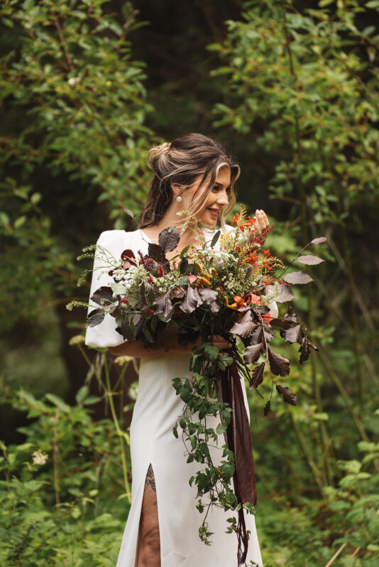 Bride holding a loose bouquet with warm-toned flowers and trailing foliage