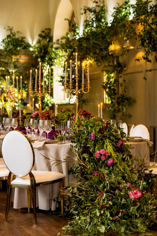 Wedding venue styling with rich pink flowers, trailing foliage and gold candelabras