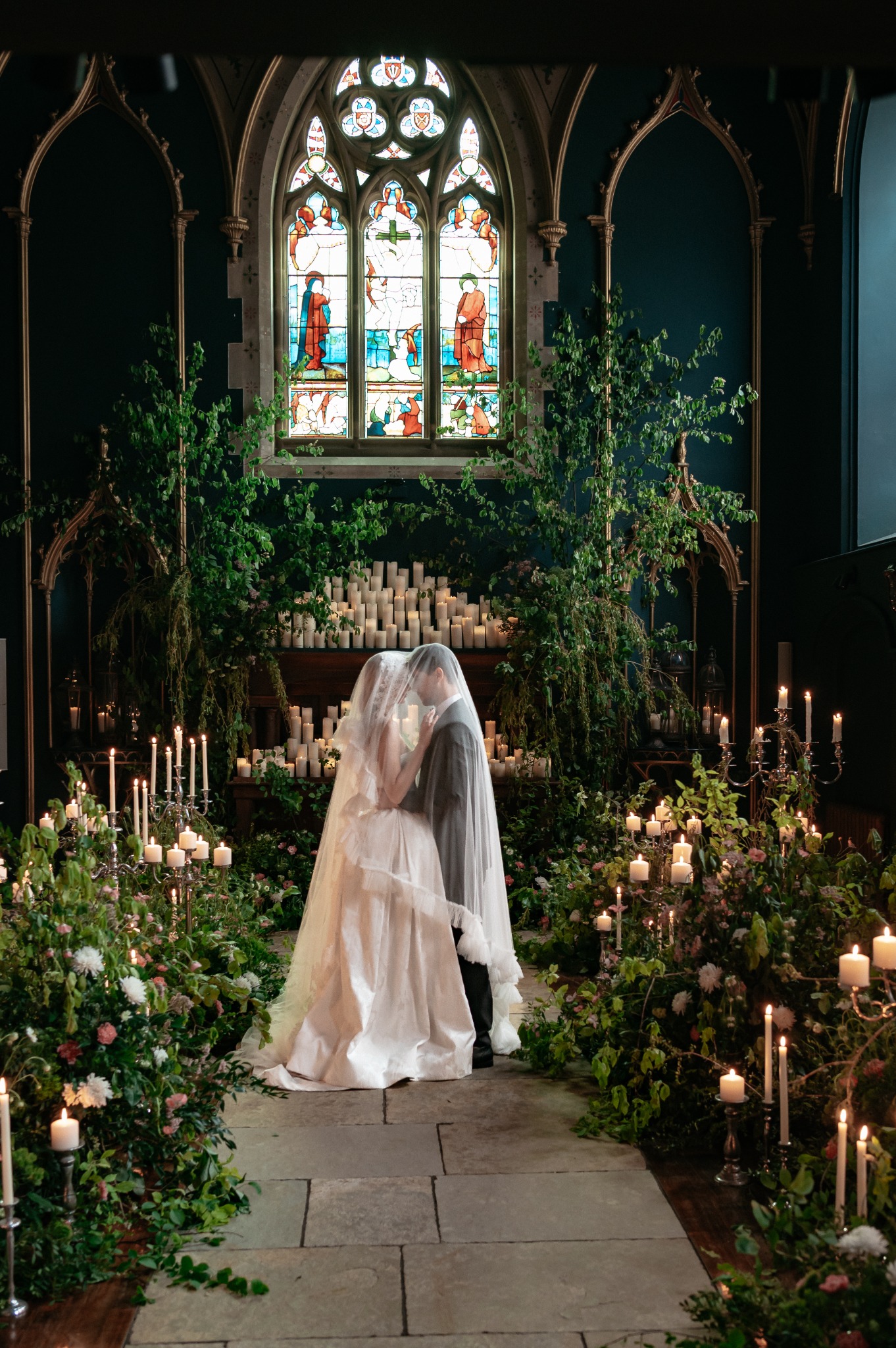 Bride in Lartington Hall chapel surrounded by flowers, foliage and candlelight